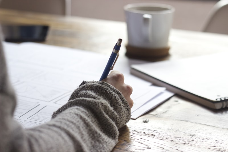 An open paper planner with a pen resting on a wooden desk in soft natural light